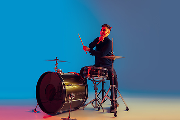 Image showing Caucasian male drummer improvising isolated on blue studio background in neon light