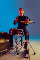 Image showing Caucasian male drummer improvising isolated on blue studio background in neon light