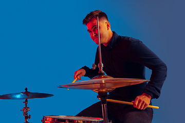 Image showing Caucasian male drummer improvising isolated on blue studio background in neon light