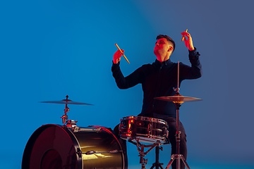 Image showing Caucasian male drummer improvising isolated on blue studio background in neon light