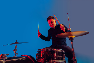 Image showing Caucasian male drummer improvising isolated on blue studio background in neon light