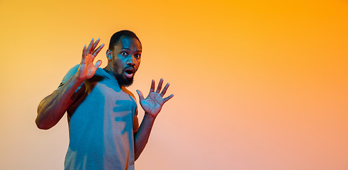 Image showing African-american man\'s portrait isolated on gradient orange studio background in neon light