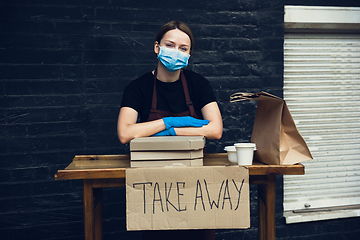 Image showing Woman preparing drinks and meals, wearing protective face mask and gloves. Contactless delivery service during quarantine coronavirus pandemic. Take away only concept.