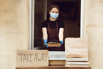 Image showing Woman preparing drinks and meals, wearing protective face mask and gloves. Contactless delivery service during quarantine coronavirus pandemic. Take away only concept.