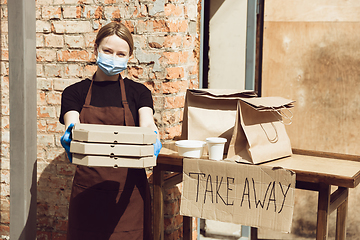 Image showing Woman preparing drinks and meals, wearing protective face mask and gloves. Contactless delivery service during quarantine coronavirus pandemic. Take away only concept.