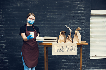 Image showing Woman preparing drinks and meals, wearing protective face mask and gloves. Contactless delivery service during quarantine coronavirus pandemic. Take away only concept.