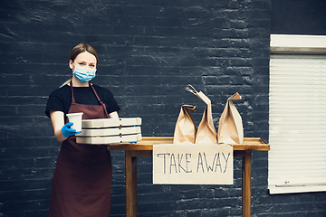 Image showing Woman preparing drinks and meals, wearing protective face mask and gloves. Contactless delivery service during quarantine coronavirus pandemic. Take away only concept.