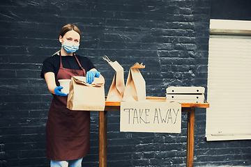 Image showing Woman preparing drinks and meals, wearing protective face mask and gloves. Contactless delivery service during quarantine coronavirus pandemic. Take away only concept.