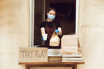 Image showing Woman preparing drinks and meals, wearing protective face mask and gloves. Contactless delivery service during quarantine coronavirus pandemic. Take away only concept.