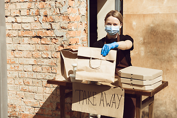 Image showing Woman preparing drinks and meals, wearing protective face mask and gloves. Contactless delivery service during quarantine coronavirus pandemic. Take away only concept.