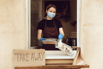 Image showing Woman preparing drinks and meals, wearing protective face mask and gloves. Contactless delivery service during quarantine coronavirus pandemic. Take away only concept.