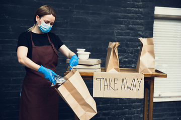 Image showing Woman preparing drinks and meals, wearing protective face mask and gloves. Contactless delivery service during quarantine coronavirus pandemic. Take away only concept.