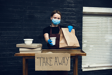 Image showing Woman preparing drinks and meals, wearing protective face mask and gloves. Contactless delivery service during quarantine coronavirus pandemic. Take away only concept.