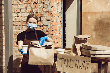 Image showing Woman preparing drinks and meals, wearing protective face mask and gloves. Contactless delivery service during quarantine coronavirus pandemic. Take away only concept.