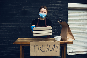 Image showing Woman preparing drinks and meals, wearing protective face mask and gloves. Contactless delivery service during quarantine coronavirus pandemic. Take away only concept.