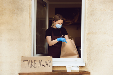 Image showing Woman preparing drinks and meals, wearing protective face mask and gloves. Contactless delivery service during quarantine coronavirus pandemic. Take away only concept.