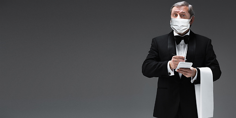 Image showing Elegance senior man waiter in protective face mask on gray background. Flyer with copyspace.