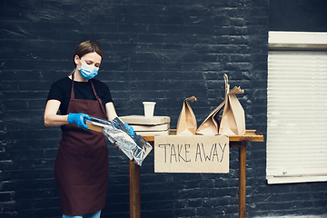 Image showing Woman preparing drinks and meals, wearing protective face mask and gloves. Contactless delivery service during quarantine coronavirus pandemic. Take away only concept.