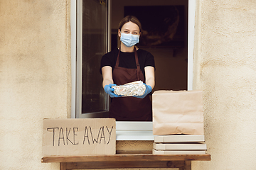 Image showing Woman preparing drinks and meals, wearing protective face mask and gloves. Contactless delivery service during quarantine coronavirus pandemic. Take away only concept.