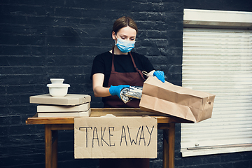 Image showing Woman preparing drinks and meals, wearing protective face mask and gloves. Contactless delivery service during quarantine coronavirus pandemic. Take away only concept.