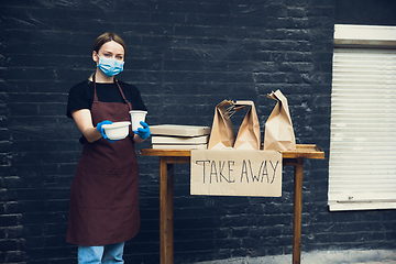 Image showing Woman preparing drinks and meals, wearing protective face mask and gloves. Contactless delivery service during quarantine coronavirus pandemic. Take away only concept.