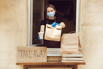 Image showing Woman preparing drinks and meals, wearing protective face mask and gloves. Contactless delivery service during quarantine coronavirus pandemic. Take away only concept.