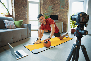 Image showing Young caucasian man training at home during quarantine of coronavirus outbreak, doing exercises of fitness, aerobic. Staying sportive during insulation.