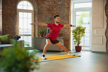 Image showing Young caucasian man training at home during quarantine of coronavirus outbreak, doing exercises of fitness, aerobic. Staying sportive during insulation.