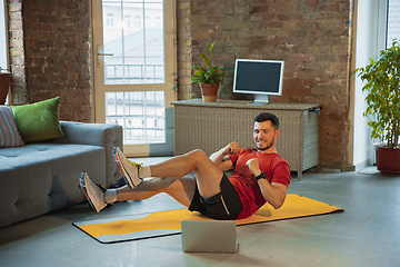 Image showing Young caucasian man training at home during quarantine of coronavirus outbreak, doing exercises of fitness, aerobic. Staying sportive during insulation.