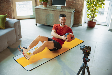 Image showing Young caucasian man training at home during quarantine of coronavirus outbreak, doing exercises of fitness, aerobic. Staying sportive during insulation.