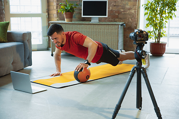 Image showing Young caucasian man training at home during quarantine of coronavirus outbreak, doing exercises of fitness, aerobic. Staying sportive during insulation.