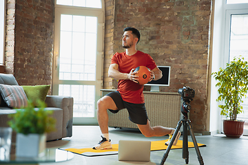 Image showing Young caucasian man training at home during quarantine of coronavirus outbreak, doing exercises of fitness, aerobic. Staying sportive during insulation.