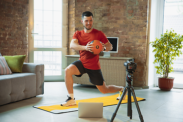 Image showing Young caucasian man training at home during quarantine of coronavirus outbreak, doing exercises of fitness, aerobic. Staying sportive during insulation.