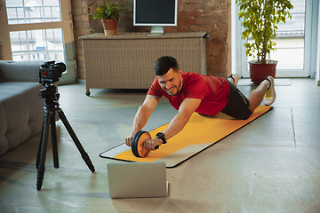 Image showing Young caucasian man training at home during quarantine of coronavirus outbreak, doing exercises of fitness, aerobic. Staying sportive during insulation.