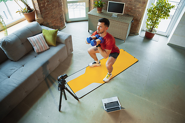 Image showing Young caucasian man training at home during quarantine of coronavirus outbreak, doing exercises of fitness, aerobic. Staying sportive during insulation.