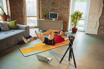 Image showing Young caucasian man training at home during quarantine of coronavirus outbreak, doing exercises of fitness, aerobic. Staying sportive during insulation.