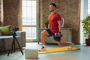 Image showing Young caucasian man training at home during quarantine of coronavirus outbreak, doing exercises of fitness, aerobic. Staying sportive during insulation.