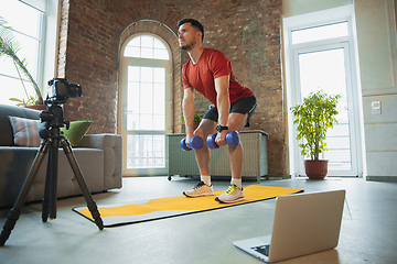 Image showing Young caucasian man training at home during quarantine of coronavirus outbreak, doing exercises of fitness, aerobic. Staying sportive during insulation.