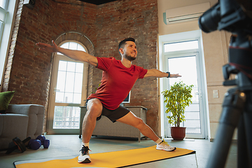 Image showing Young caucasian man training at home during quarantine of coronavirus outbreak, doing exercises of fitness, aerobic. Staying sportive during insulation.