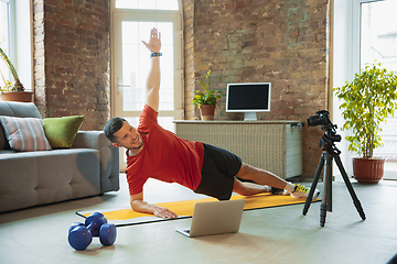 Image showing Young caucasian man training at home during quarantine of coronavirus outbreak, doing exercises of fitness, aerobic. Staying sportive during insulation.