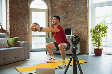 Image showing Young caucasian man training at home during quarantine of coronavirus outbreak, doing exercises of fitness, aerobic. Staying sportive during insulation.