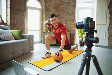 Image showing Young caucasian man training at home during quarantine of coronavirus outbreak, doing exercises of fitness, aerobic. Staying sportive during insulation.