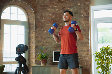 Image showing Young caucasian man training at home during quarantine of coronavirus outbreak, doing exercises of fitness, aerobic. Staying sportive during insulation.