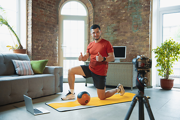 Image showing Young caucasian man training at home during quarantine of coronavirus outbreak, doing exercises of fitness, aerobic. Staying sportive during insulation.