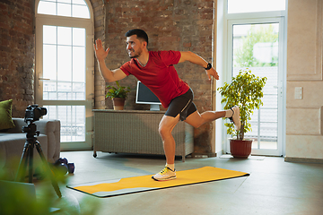 Image showing Young caucasian man training at home during quarantine of coronavirus outbreak, doing exercises of fitness, aerobic. Staying sportive during insulation.