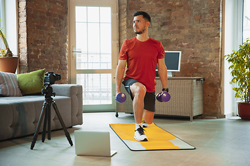 Image showing Young caucasian man training at home during quarantine of coronavirus outbreak, doing exercises of fitness, aerobic. Staying sportive during insulation.