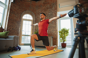 Image showing Young caucasian man training at home during quarantine of coronavirus outbreak, doing exercises of fitness, aerobic. Staying sportive during insulation.