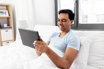 Image showing happy indian man with tablet pc in bed at home