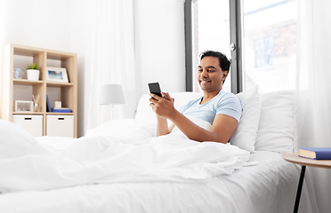 Image showing happy indian man with smartphone in bed at home