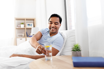 Image showing happy indian man drinking water lying in bed